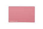 A rectangular dusky pink beauty mat with rounded corners and the text 'THE BEAUTY MAT' printed in white at the bottom left, shown on a plain white background.