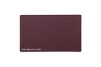 A rectangular maroon beauty mat with rounded corners and the text 'THE BEAUTY MAT' printed in white at the bottom left, shown on a plain white background.