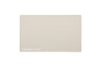 A rectangular oatmeal beige beauty mat with rounded corners and the text 'THE BEAUTY MAT' printed in white at the bottom left, shown on a solid white background.