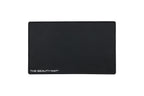 A black rectangular beauty mat with rounded corners and the text 'THE BEAUTY MAT' printed in white at the bottom left, shown on a plain white background.